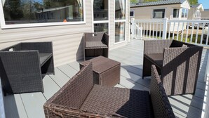 Una terraza techada al aire libre con mobiliario de mimbre, ventanas amplias y barandilla blanca.