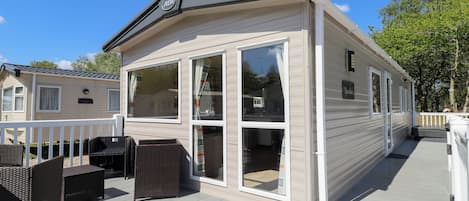 A mobile home with a deck, wicker furniture, and large windows.