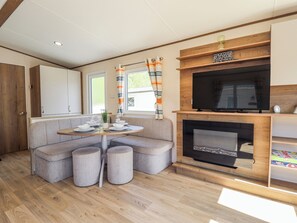 A compact living space with a sofa, a small round table set for dining, a television, and a fireplace. - 39 Larch View With hot tub (Lincoln)