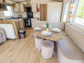 A compact kitchen with modern appliances, a dining area with a wooden table and cushioned seating, and a window providing natural light.