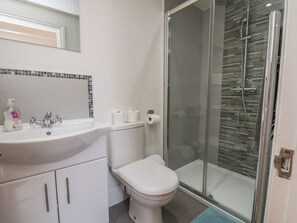 A bathroom with a white sink, toilet, and glass shower enclosure. - Reighton House (Filey)