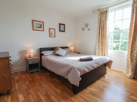 Un dormitorio con cama, mesitas de noche, cómoda y ventana con cortinas.