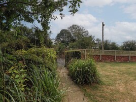 Un sendero de jardín que lleva a una entrada con portón, rodeado de follaje denso y un muro de ladrillo.