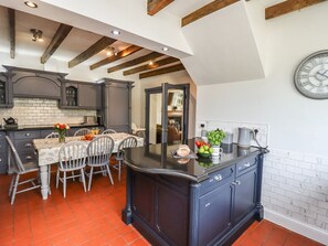 A kitchen with dark cabinetry, a central island, and a dining area with chairs. - Reighton House (Filey)