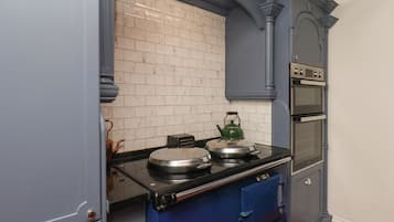 Una cocina con estufa negra, hervidor verde y salpicadero de azulejos blancos.