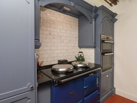 Una cocina con estufa negra, hervidor verde y salpicadero de azulejos blancos.