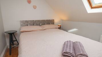 A bedroom with a bed, pillows, a nightstand, a lamp, and a window.