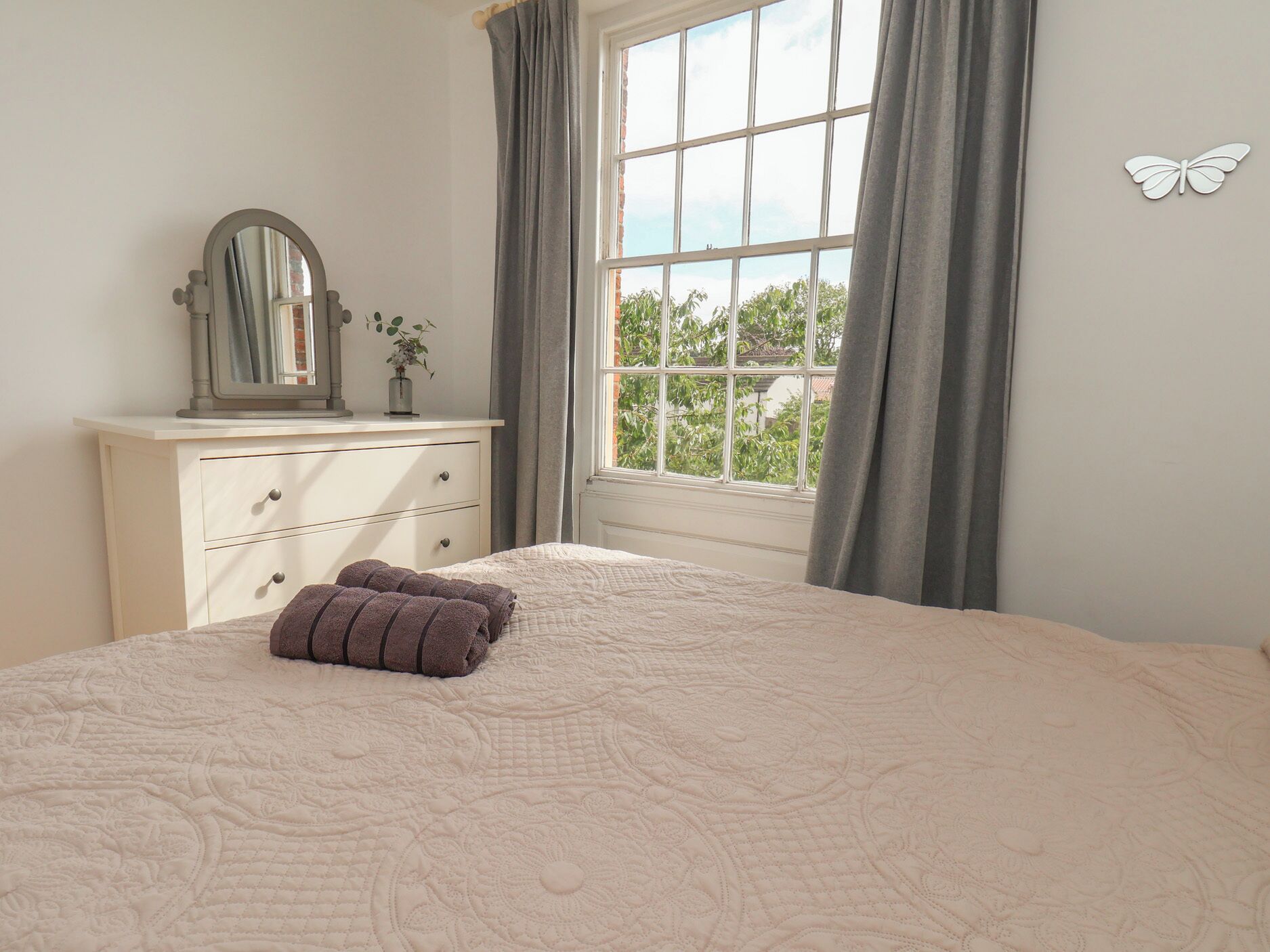 Une chambre à coucher avec un grand lit, une commode, un miroir et une fenêtre avec des rideaux.