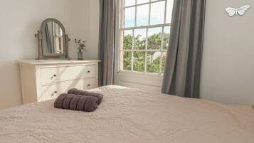 A bedroom with a large bed, a dresser, a mirror, and a window with curtains.