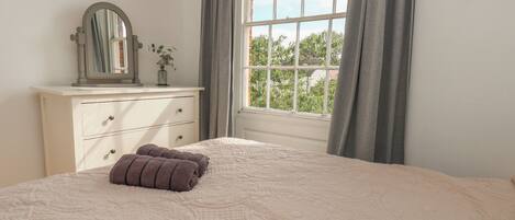 Une chambre à coucher avec un grand lit, une commode, un miroir et une fenêtre avec des rideaux.