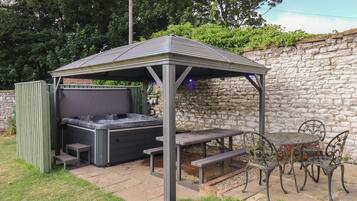 A covered outdoor seating area with a hot tub, picnic tables, and metal chairs.