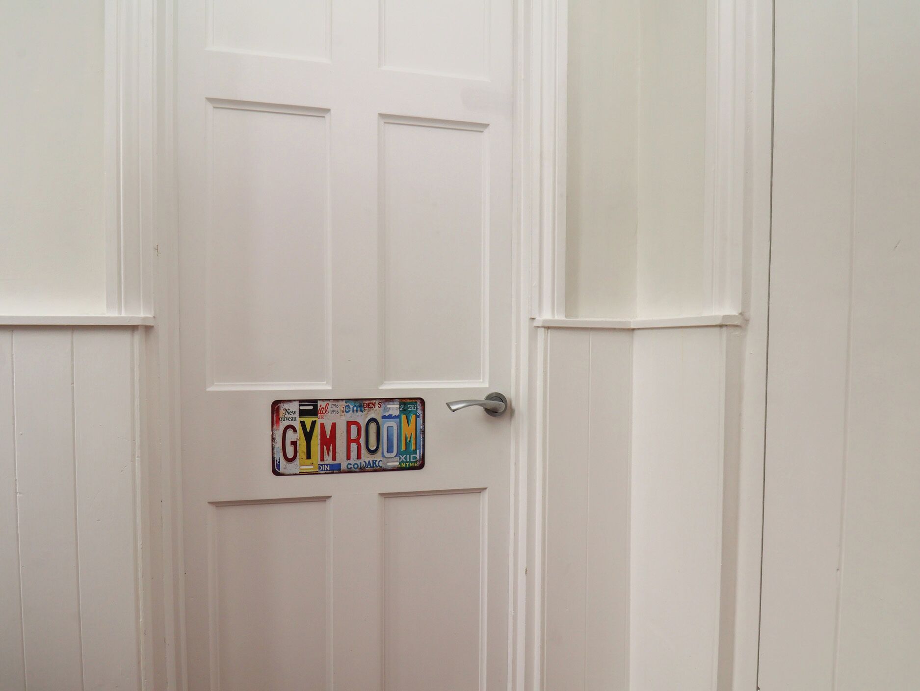 Una puerta blanca con una placa que dice 'GYMROOM'.