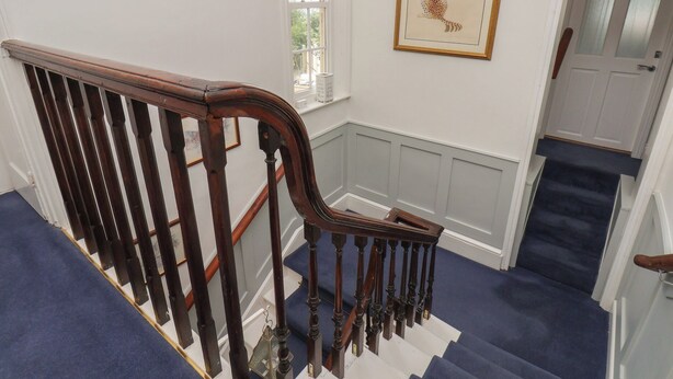 A staircase with a wooden handrail and blue carpeted steps leading to a landing. - Reighton House (Filey)