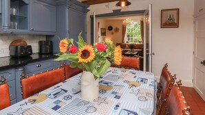 A dining area with a table set for four, a vase of sunflowers, and a view into a living room with a sofa and a window. - Reighton House (Filey)