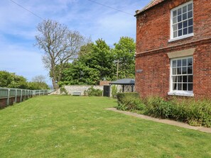 A brick building with a garden, a stone wall, and a bench. - Reighton House (Filey)