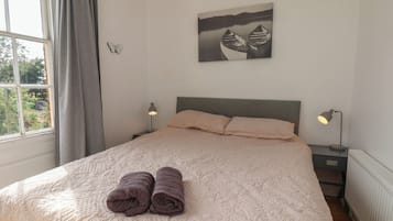 A bedroom with a bed, two bedside lamps, a window with curtains, and a wall-mounted picture.