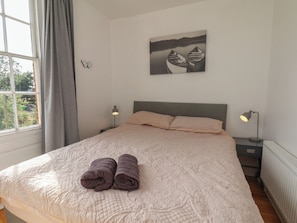 Un dormitorio con una cama, dos lámparas de noche, una ventana con cortinas y un cuadro en la pared.