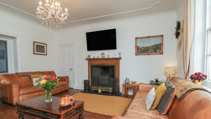 A living room with leather sofas, a wooden coffee table, a fireplace, a television, and a chandelier. - Reighton House (Filey)
