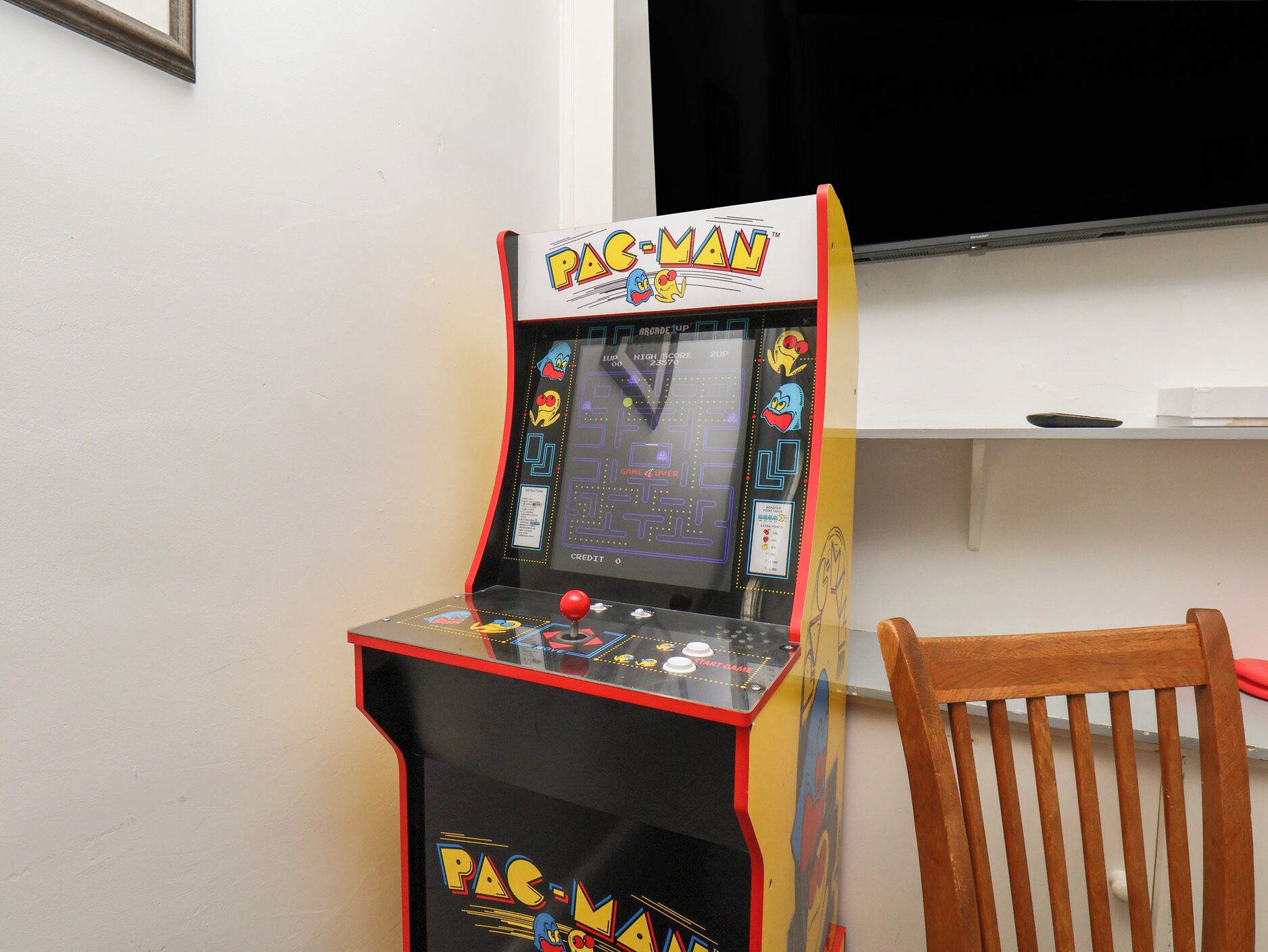 A Pac-Man arcade machine with a score display, placed next to a wooden chair.