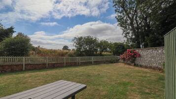 A picnic table in a grassy backyard with a stone wall and a wooden fence.