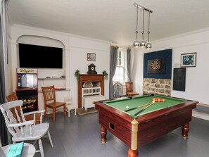 Una sala de billar con mesa de pool, sillas, televisor y dardos.