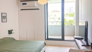 Ein modernes Schlafzimmer mit Bett, Schreibtisch, Stuhl, Fenster und Klimaanlage.