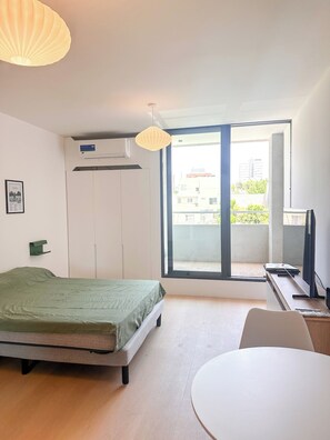 Une chambre moderne comprenant un lit, un bureau, une chaise, une fenêtre et un appareil de climatisation.