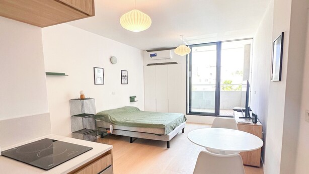 Eine moderne Küche mit Einbauherd, einem Esstisch mit Stühlen, einem Bett und einem großen Fenster.