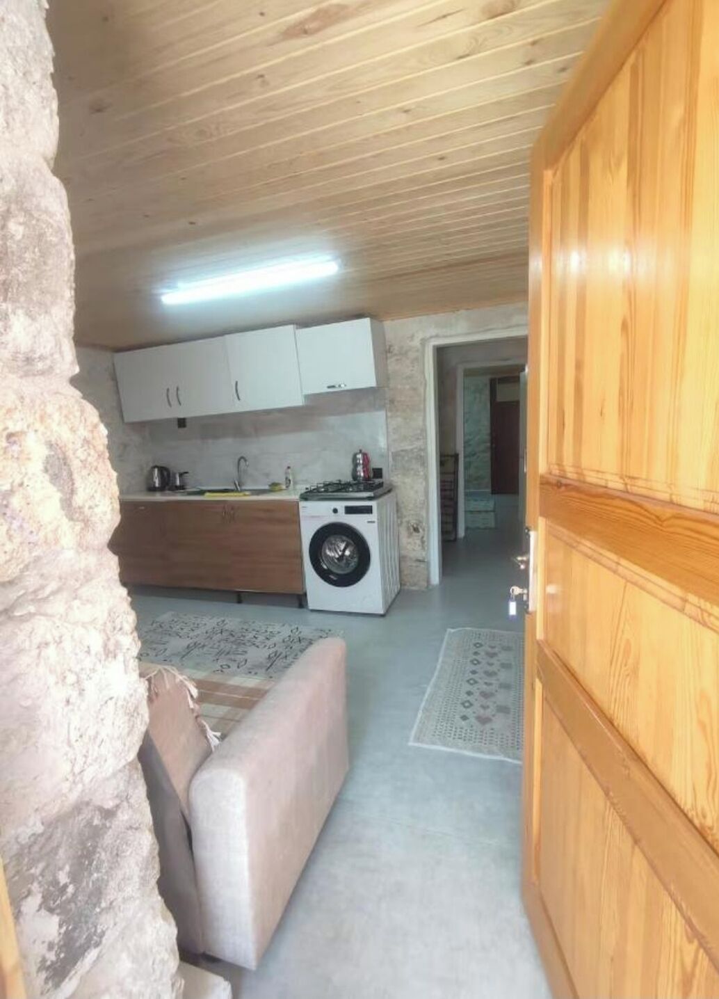 Een kleine keuken met een wasmachine, een bank en een houten garderobe.