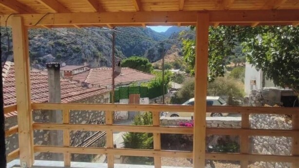 Un balcon en bois offrant une vue sur un paysage montagneux et des bâtiments aux toits de tuiles rouges.