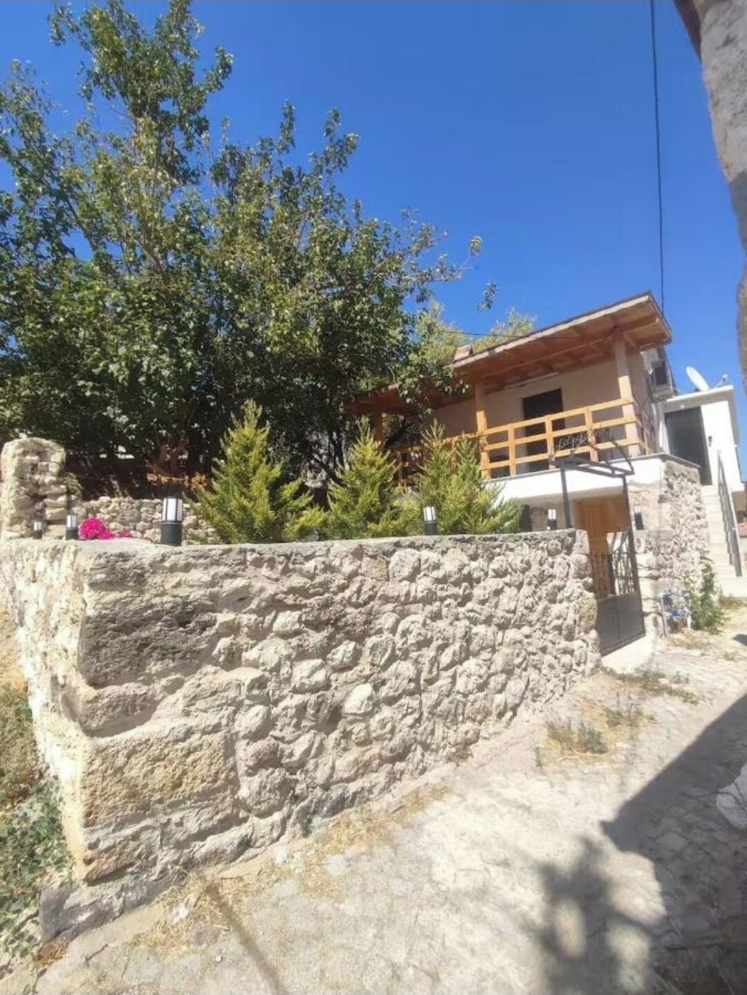 A stone wall, a wooden building with a balcony, and a clear blue sky.