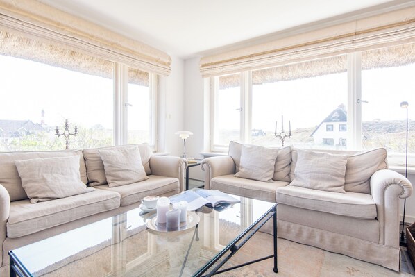 A room with two sofas, a glass coffee table, and large windows with curtains.
