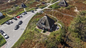 Een kustdorp met traditionele huizen met rieten daken, een parkeerplaats en een weg die naar de zee leidt.