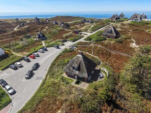 Un pueblo costero con casas tradicionales de techo de paja, un aparcamiento y un camino que lleva al mar.