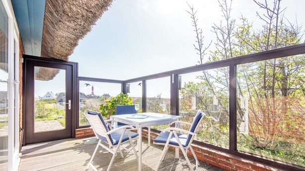 Een terras met een tafel, stoelen, een glazen deur en uitzicht op bomen en gebouwen.