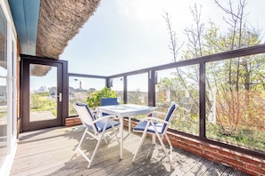 A patio with a table and chairs, a glass door, and a view of trees and buildings.