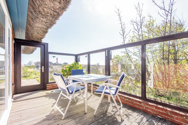 Un patio con una mesa y sillas, un ventanal de vidrio y vistas a árboles y edificios.
