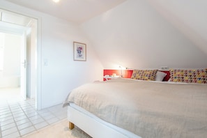 A bedroom with a bed, a bedside table, a lamp, and a door leading to another room.