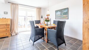 Een eetgedeelte met een houten tafel, twee stoelen, een vaas met bloemen en een schilderij aan de muur.