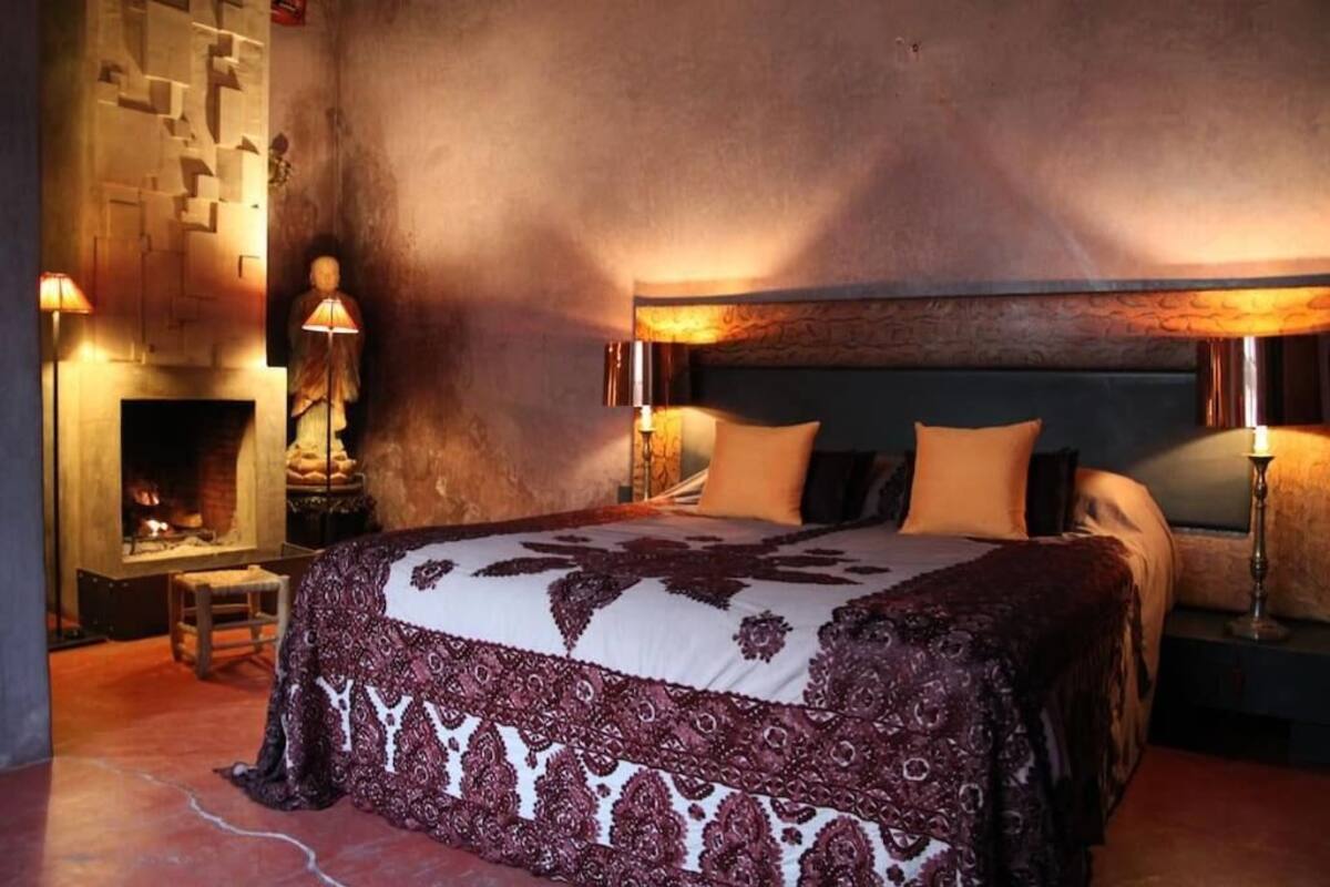 A bedroom with a large bed, a fireplace, and a stone wall.