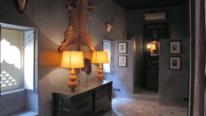 Een gang met een groot dierenhuid aan de muur, een houten kast met lampen, en ingelijste foto's.