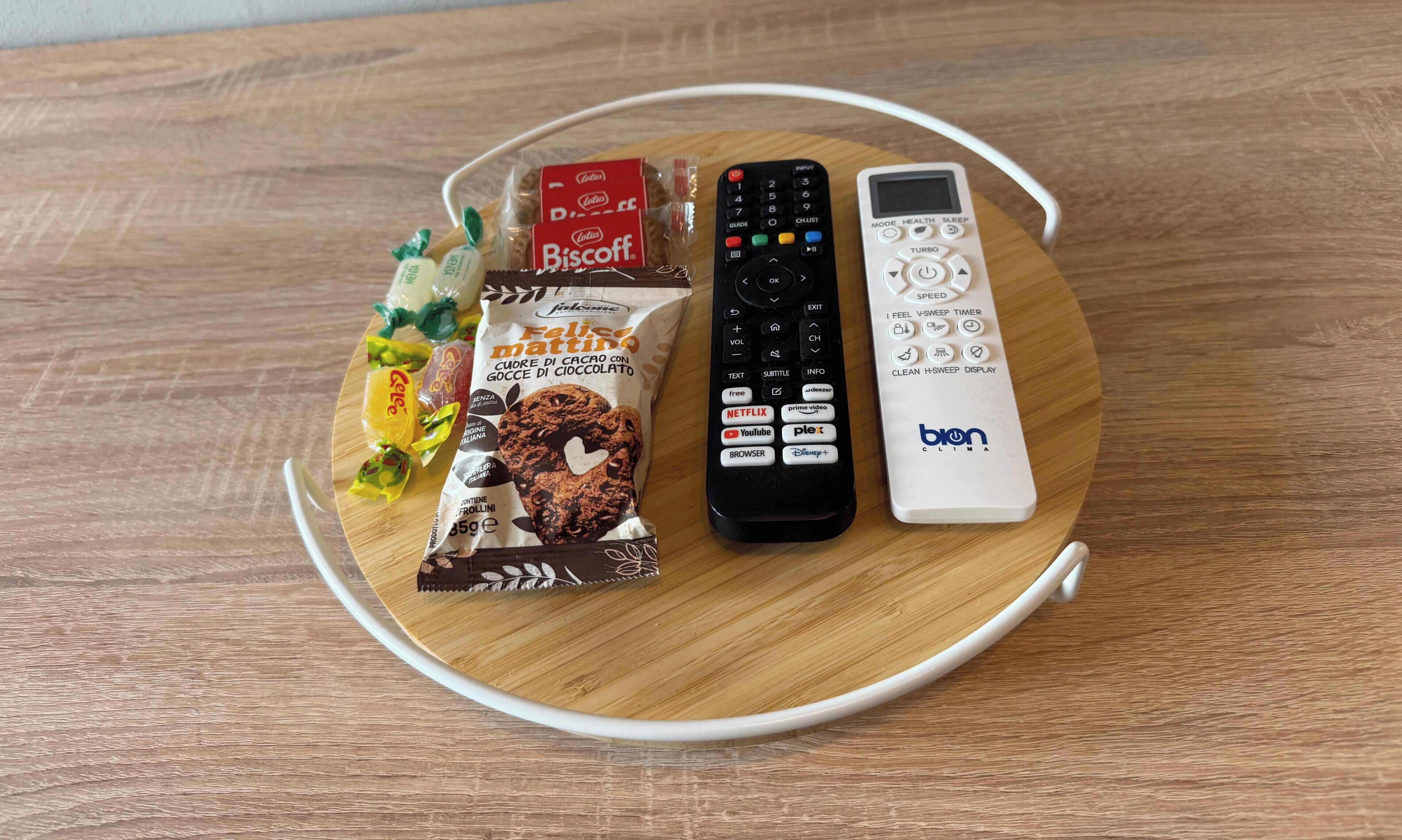 A tray with snacks, a black remote control, and a white remote control on a wooden surface.