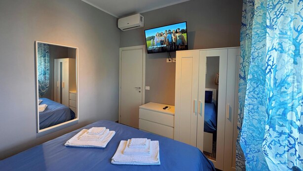Habitación de hotel con cama, televisión montada en la pared, armario y baño visible a través de una puerta abierta.