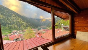 Interior de madera con un amplio ventanal que da a un pueblo y montañas.