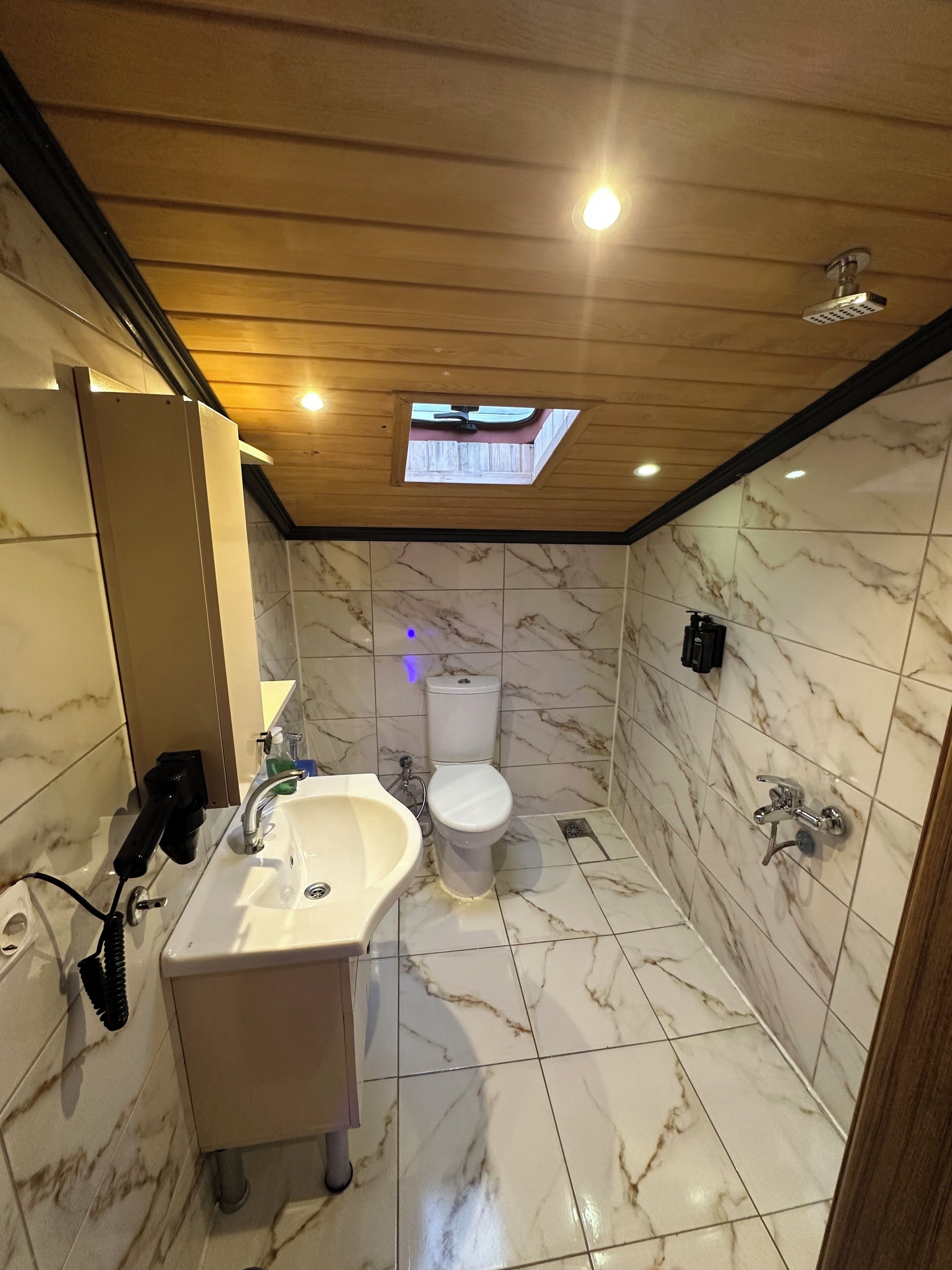 A bathroom with a marble floor, a sink, a toilet, and a shower.