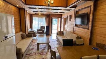 Una habitación con techo de madera, una mesa de comedor con sillas, un sofá, un televisor montado en la pared y un refrigerador.