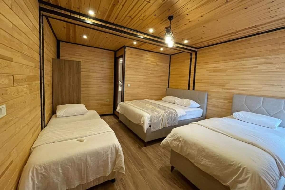 A room with three beds, wooden walls, and a ceiling fan.
