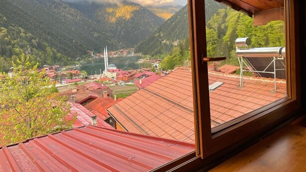 Una habitación con vista a un paisaje montañoso, un edificio de techos rojos y una ventana con reja de metal.