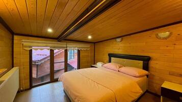 Un dormitorio con techo de madera, una cama con ropa de cama rosa, una mesita de noche y una ventana con vistas.