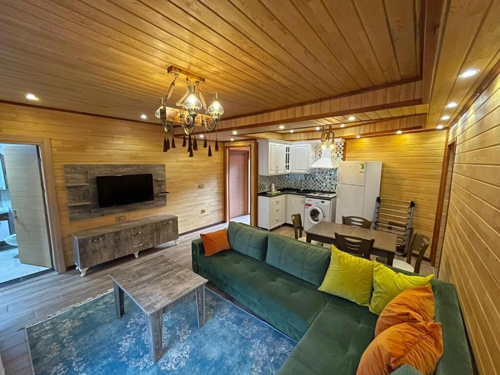 A cozy living area with a green sofa, wooden ceiling, built-in TV, and a kitchen in the background.